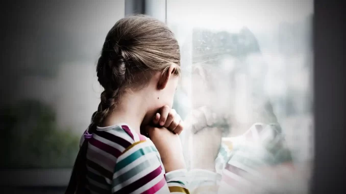 Barn står vid ett fönster , deprimerad