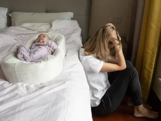 Kvinna sitter vid sidan av sängen ledsen. Ett barn ligger på sängen
