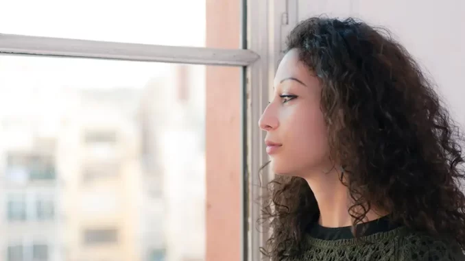 Kvinna tittar ut genom ett fönster hoppfullt