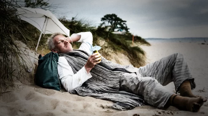 Fattig person ligger på en strand och dricker en paraplydrink